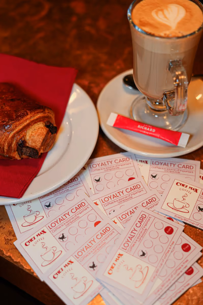 Cartes de fidélité Chez Max posées près d'un café et d'un pain au chocolat